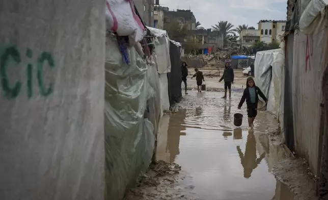 Palestinian children carry buckets of water after overnight rainfall at the refugee tent camp for displaced Palestinians in Deir al-Balah, central Gaza Strip, Tuesday, Dec. 31, 2024. (AP Photo/Abdel Kareem Hana)