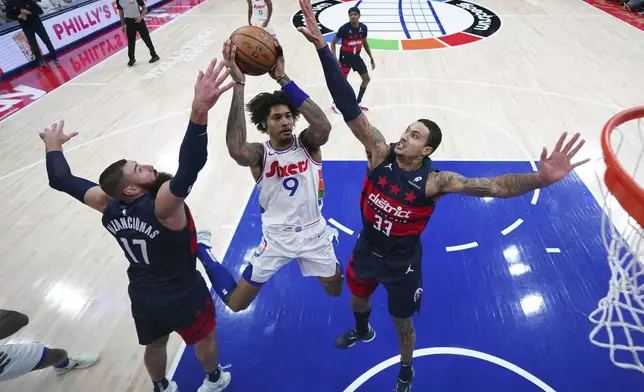 Philadelphia 76ers' Kelly Oubre Jr., center, goes up for a shot between Washington Wizards' Kyle Kuzma, right, and Jonas Valanciunas during the first half of an NBA basketball game, Wednesday, Jan. 8, 2025, in Philadelphia. (AP Photo/Matt Slocum)