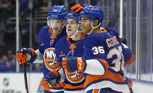 New York Islanders center Mathew Barzal, center, is congratulated by defensemen Scott Mayfield (24) and Isaiah George (36) during the second period of an NHL hockey game against the San Jose Sharks, Saturday, Jan. 18, 2025, in Elmont, N.Y. (AP Photo/Corey Sipkin).