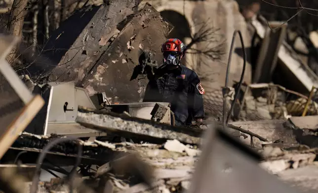 A member of a San Bernardino County Fire Department Search and Rescue crew works among the ruins of the Palisades Fire in the Pacific Palisades neighborhood of Los Angeles, Tuesday, Jan. 14, 2025. (AP Photo/Carolyn Kaster)
