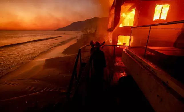 Firefighters work from a deck as the Palisades Fire burns a beachfront property Jan. 8, 2025, in Malibu, Calif. (AP Photo/Etienne Laurent)