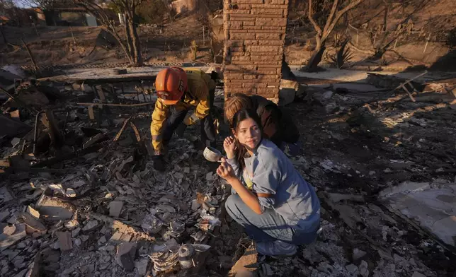 Ella Venne, front, holds a cup she found in the remains of her family's home destroyed by the Eaton Fire as she searches with Glendale Fire Department captain Chris Jernegan, left, and his wife Alison in Altadena, Calif., Saturday, Jan. 11, 2025. (AP Photo/Mark J. Terrill)