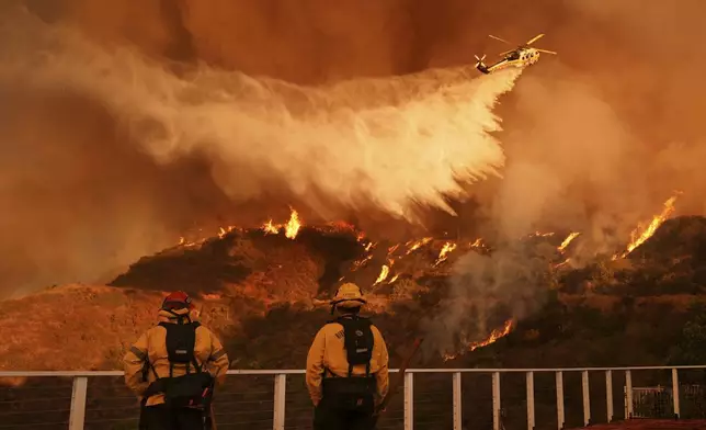 Firefighters watch as water is dropped on the Palisades Fire in Mandeville Canyon Saturday, Jan. 11, 2025, in Los Angeles. (AP Photo/Jae C. Hong)