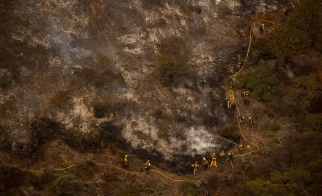 A group of firefighters traverse a steep hill while battling the Palisades Fire in the Mandeville Canyon neighborhood of Los Angeles, Calif., Saturday, Jan. 11, 2025. (Stephen Lam/San Francisco Chronicle via AP)