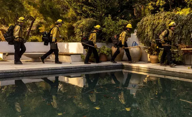 A Cal Fire hand crew walks past a swimming pool toward their next assignment during the Palisades Fire in the Mandeville Canyon neighborhood of Los Angeles, Calif., Saturday, Jan. 11, 2025. (Stephen Lam/San Francisco Chronicle via AP)