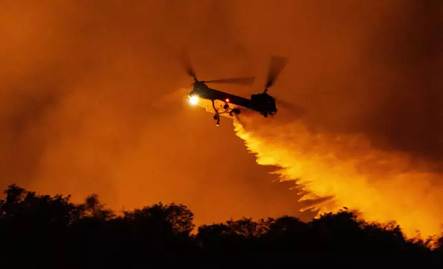 A helicopter drops water on the Palisades Fire in Mandeville Canyon, Saturday, Jan. 11, 2025, in Los Angeles.(AP Photo/Etienne Laurent)