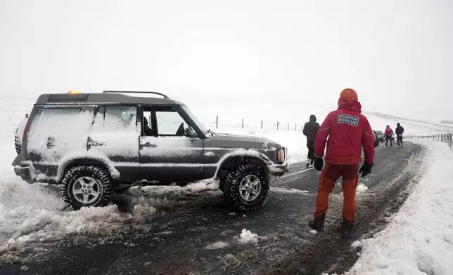 A member of a Mountain Rescue team stand on a road after helping to clear cars from a snow drift near Ribblehead, England, Monday, Jan. 6, 2025. (Danny Lawson/PA via AP)