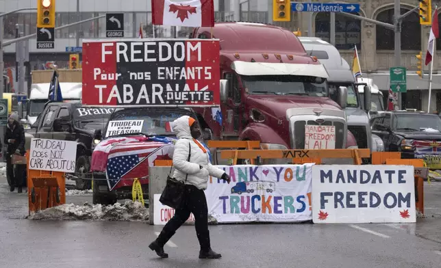 FILE - A woman crosses the street in front of vehicles parked as part of the trucker protest, on Feb. 8, 2022 in Ottawa. Canadian lawmakers expressed increasing worry about protests over vaccine mandates other other COVID restrictions after the busiest border crossing between the U.S. and Canada became partially blocked. (Adrian Wyld /The Canadian Press via AP, File)