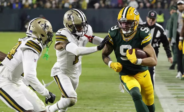 Green Bay Packers wide receiver Christian Watson (9) carries against New Orleans Saints cornerback Alontae Taylor (1) during the first half of an NFL football game, Monday, Dec. 23, 2024, in Green Bay, Wis. (AP Photo/Mike Roemer)