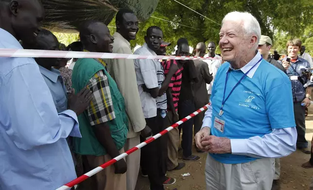 FILE - Former U.S. President Jimmy Carter, right, greets Southern Sudanese men waiting to cast their vote at a polling station in Juba, Southern Sudan, Jan 9, 2011, during a weeklong referendum on independence that is expected to split Africa's largest nation in two. (AP Photo/Jerome Delay, File)