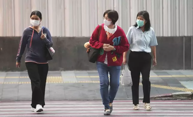 Women wear sweater cross a street in Bangkok, Thailand, Thursday, Jan. 16, 2025. (AP Photo/Sakchai Lalit)
