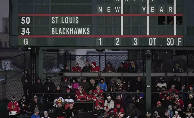 Fans sit underneath the scoreboard before NHL Winter Classic outdoor hockey game featuring the Chicago Blackhawks and St. Louis Blues at Wrigley Field, Tuesday, Dec. 31, 2024, in Chicago. (AP Photo/Erin Hooley)