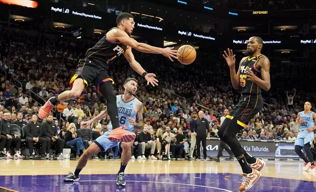 Phoenix Suns guard Devin Booker, left, passes the ball to Kevin Durant, right, as Memphis Grizzlies guard John Konchar, middle, watches during the second half of an NBA basketball game Tuesday, Dec. 31, 2024, in Phoenix. Memphis won 117-112. (AP Photo/Darryl Webb)