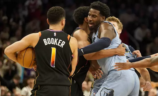 Phoenix Suns forward Ryan Dunn, center, holds back Memphis Grizzlies forward Jaren Jackson Jr., right, as Jackson goes after Devin Booker (1) during the second half of an NBA basketball game Tuesday, Dec. 31, 2024, in Phoenix. (AP Photo/Darryl Webb)