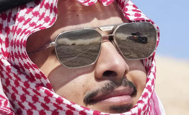 A car is reflected in the glasses of a spectator during the ninth stage of the Dakar Rally between Riyadh and Haradh, Saudi Arabia, Tuesday, Jan. 14, 2025. (AP Photo/Christophe Ena)