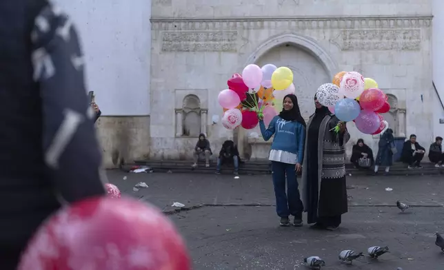 People pose for photos with balloons near Al-Hamidiyeh Souq on New Years Eve in Damascus, Syria, Tuesday, Dec. 31, 2024 (AP Photo/Mosa'ab Elshamy)