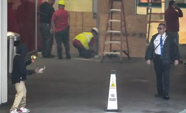 A private security guard, right, keeps a man suffering homelessness away as workers secure the outside of a temporarily closed Target store after two security guards were shot and wounded after they confronted a man suspected of shoplifting in downtown Los Angeles on Tuesday, Dec. 31, 2024. (AP Photo/Damian Dovarganes)