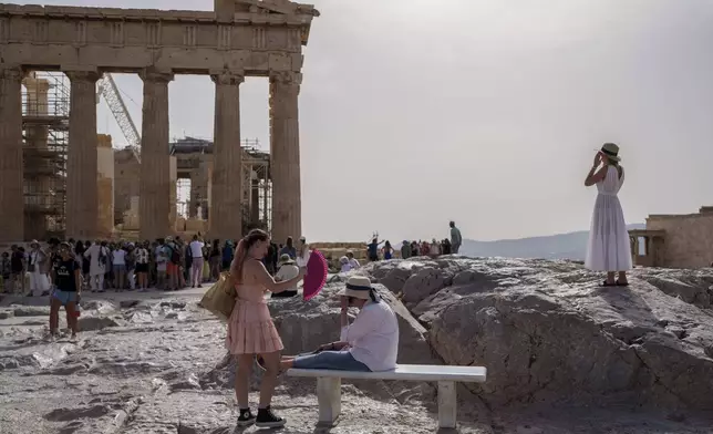 FILE - A tourist uses a hand fan to cool down another one sitting on a bench in front of the Parthenon at the ancient Acropolis, in Athens, June 12, 2024. (AP Photo/Petros Giannakouris, File)