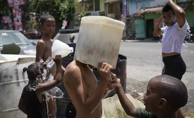 FILE - A child covers his head with a bucket on a hot day in the Los Guandules neighborhood of Santo Domingo, Dominican Republic, May 20, 2024. (AP Photo/Matias Delacroix, File)