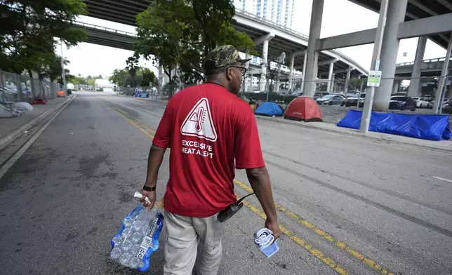 FILE - Ricky Leath, an outreach specialist with the City of Miami, walks through a homeless encampment as he works with the Miami-Dade County Homeless Trust to distribute bottles of water and other supplies to the homeless population, helping them manage high temperatures, May 15, 2024, in Miami. (AP Photo/Lynne Sladky, File)