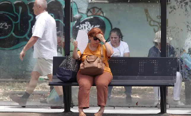 FILE - A woman tries to cool herself while waiting for a bus on a hot day in Skopje, North Macedonia, June 20, 2024. (AP Photo/Boris Grdanoski, File)