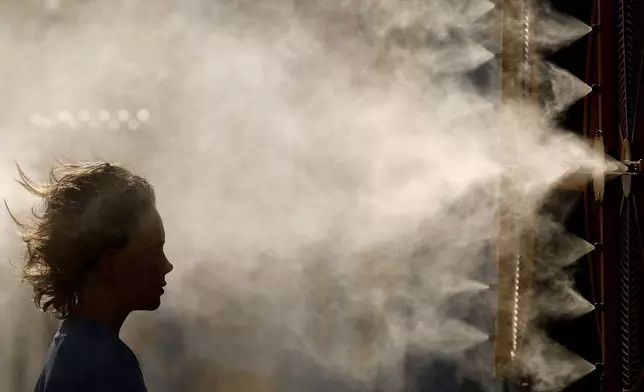 FILE - Michael Mullenax, 10, from Lee's Summit, Mo., cools off in a mister at Kauffman Stadium before a baseball game between the Kansas City Royals and the Miami Marlins, June 24, 2024, in Kansas City, Mo. (AP Photo/Charlie Riedel, File)