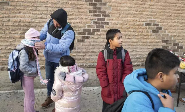 Gabriel Montilla waits for a bus with his children after picking up his children from their school in the Flatbush neighborhood of Brooklyn and commuting with them to a shelter in the Jamaica neighborhood of the Queens borough of New York, Tuesday, Jan. 14, 2025. Montilla and his family were recently relocated to a migrant shelter in Queens after the family shelter at Floyd Bennett Field was closed. (AP Photo/Klaus Galiano)
