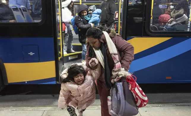 Ecuadorian Leidy Andrade consoles her daughter as they alight from a bus during their commute from Brooklyn to the Queens borough of New York, Tuesday, Jan. 14, 2025. Andrade and her family were recently relocated to the shelter in Queens after the family shelter at Floyd Bennett Field was closed. (AP Photo/Klaus Galiano)