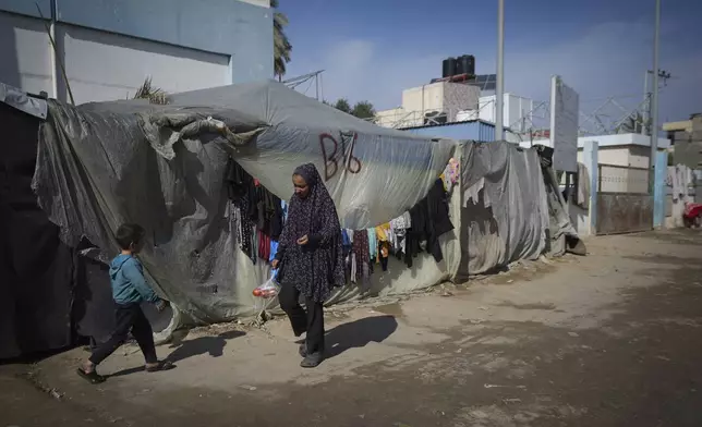 A woman and a child walk outside their tent at a camp for displaced Palestinians in Deir al-Balah, central Gaza Strip, Friday Jan. 17, 2025. (AP Photo/Abdel Kareem Hana)