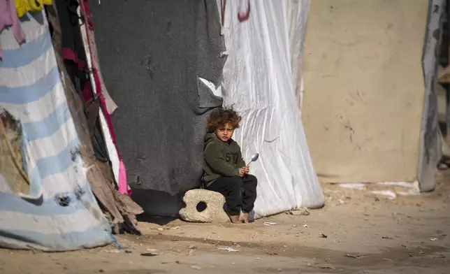 A child sits outside a tent at a camp for displaced Palestinians in Deir al-Balah, central Gaza Strip, Friday Jan. 17, 2025. (AP Photo/Abdel Kareem Hana)