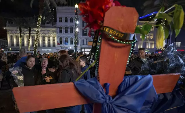 Jessica Perez, holding flowers left, hugs her mother Martha Perez who cries out by a cross memorializing her daughter, Nicole Perez, who was a victim on the New Year's Day attack, on Canal Street near the intersection of Bourbon Street in New Orleans, Saturday, Jan. 4, 2025. (AP Photo/Matthew Hinton)