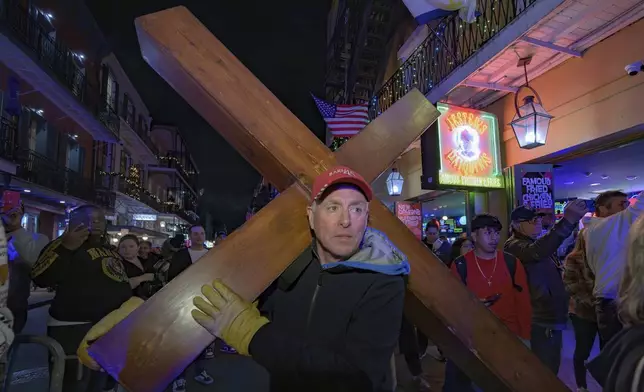 Dan Beazley, of Northville, Mich., walks with a cross in front of a parade on Bourbon Street in New Orleans, Saturday, Jan. 4, 2025, as they memorialize the victims of the New Year's Day deadly truck attack and shooting. (AP Photo/Matthew Hinton)