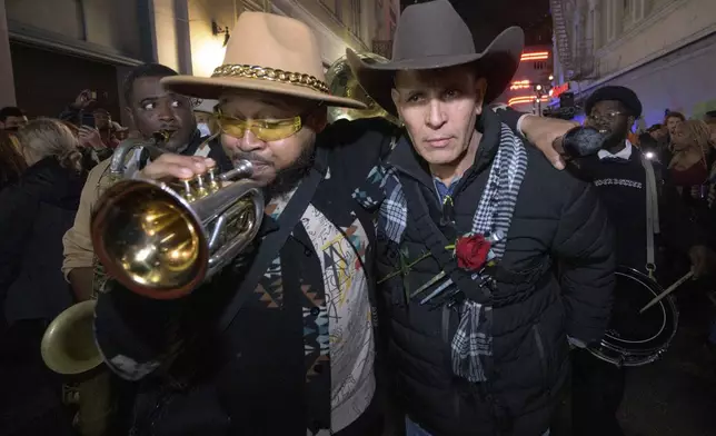 Amir "Tubad" Gray, left, leads Tubad and the Kings of NOLA Brass Band and artist Roberto Marquez, right, in New Orleans, Saturday, Jan. 4, 2025, as they memorialize the victims of the New Year's Day deadly truck attack and shooting. Marquez organized the parade and vigil and designed a memorial for the victims on Bourbon Street. (AP Photo/Matthew Hinton)