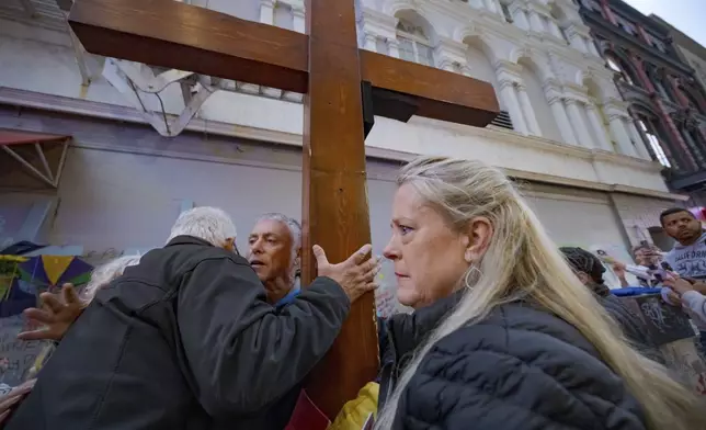 Louis Tenedorio, left, of Long Island, N.Y., hugs Dan Beazley of Northville, Mich., holding cross, as Linda Flick looks toward a memorial on Bourbon Street and Canal Street in New Orleans, Saturday, Jan. 4, 2025, where Flick's nephew and Tenedorio's son, Matthew Tenedorio, was killed in the New Year's Day attack. (AP Photo/Matthew Hinton)