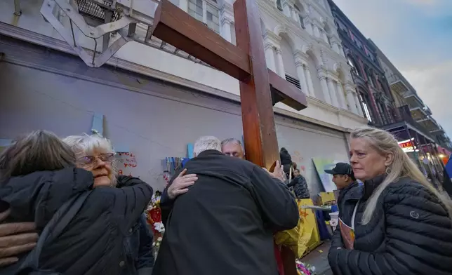 Long Island, N.Y. residents Cathy Tenedorio, second left, and Louis Tenedorio, center left, are hugged by supporters including Dan Beazley of Northville, Michigan, holding cross, as Linda Flick, right, looks toward a memorial on Bourbon Street and Canal Street in New Orleans, Saturday, Jan. 4, 2025, where Flick's nephew and the Tenedorio's son, Matthew Tenedorio, was killed in the New Year's Day attack. (AP Photo/Matthew Hinton)