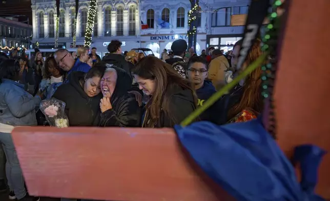 Jessica Perez, holding flowers left, hugs her mother Martha Perez who cries out by a cross memorializing her daughter, Nicole Perez, who was a victim on the New Year's Day attack, on Canal Street near the intersection of Bourbon Street in New Orleans, Saturday, Jan. 4, 2025. (AP Photo/Matthew Hinton)