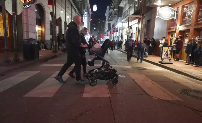 A couple pushes a child in a stroller on Bourbon Street at the site of a deadly truck attack on New Year's Day in New Orleans, Friday, Jan. 3, 2025. (AP Photo/Gerald Herbert)