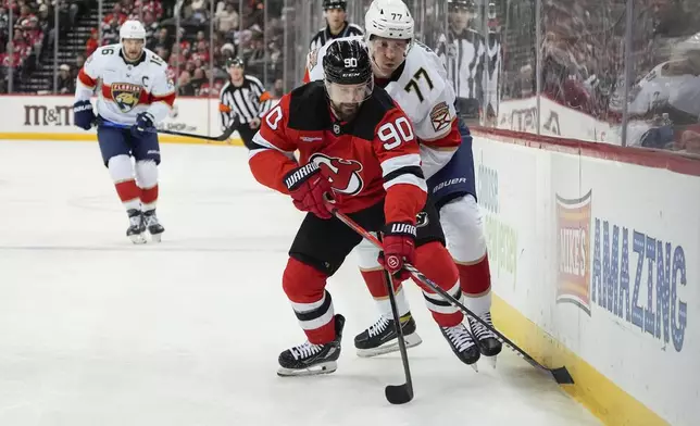 New Jersey Devils left wing Tomas Tatar (90) and Florida Panthers defenseman Niko Mikkola (77) fight for the puck during the first period of an NHL hockey game, Tuesday, Jan. 14, 2025, in Newark, N.J. (AP Photo/Julia Demaree Nikhinson)