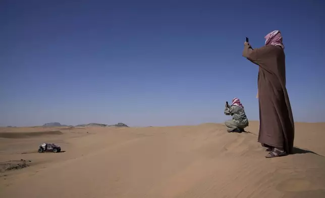 Two men take pictures of Driver Sebastien Loeb and co-driver Fabian Lurquin during the stage two, day One, of the Dakar Rally with start in Bisha and finish in Bisha, Saudi Arabia, Sunday, Jan. 5, 2025. (AP Photo/Christophe Ena)