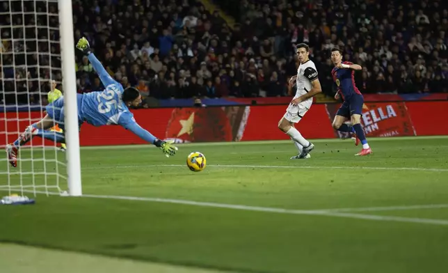Barcelona's Robert Lewandowski, right, scores his side's sixth goal past Valencia's goalkeeper Giorgi Mamardashvili during the Spanish La Liga soccer match between Barcelona and Valencia at the Lluis Companys Olympic Stadium in Barcelona, Spain, Sunday, Jan. 26, 2025. (AP Photo/Joan Monfort)