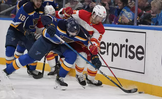 Calgary Flames' Kevin Rooney (21) and St. Louis Blues' Philip Broberg (6) chase after a loose puck along the boards during the third period of an NHL hockey game Tuesday, Jan. 14, 2025, in St. Louis. (AP Photo/Jeff Roberson)