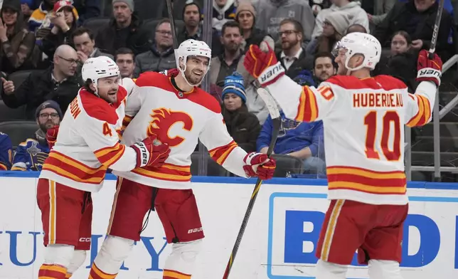 Calgary Flames' Kevin Bahl is congratulated by teammates Rasmus Andersson, left, and Jonathan Huberdeau (10) after scoring during the third period of an NHL hockey game against the St. Louis Blues Tuesday, Jan. 14, 2025, in St. Louis. (AP Photo/Jeff Roberson)