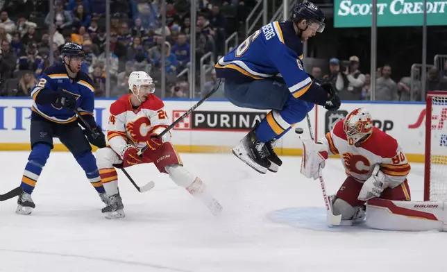 St. Louis Blues' Philip Broberg leaps over the puck as Calgary Flames' Jake Bean (24) and goaltender Dan Vladar (80) defend and Blues' Radek Faksa, left, watches during the second period of an NHL hockey game Tuesday, Jan. 14, 2025, in St. Louis. (AP Photo/Jeff Roberson)