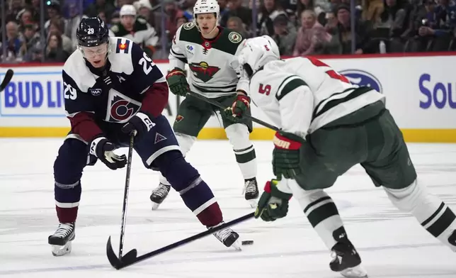 Colorado Avalanche center Nathan MacKinnon, left, loses control of the puck while driving between Minnesota Wild defenseman Jake Middleton, front right, and center Marco Rossi in the first period of an NHL hockey game Monday, Jan. 20, 2025, in Denver. (AP Photo/David Zalubowski)
