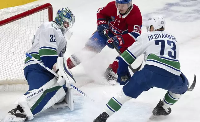 Montreal Canadiens' Emil Heineman (51) is stopped by Vancouver Canucks goaltender Kevin Lankinen (32) as Canucks' Vincent Desharnais (73) moves in to defend during first-period NHL hockey game action in Montreal, Monday, Jan. 6, 2025. (Ryan Remiorz/The Canadian Press via AP)