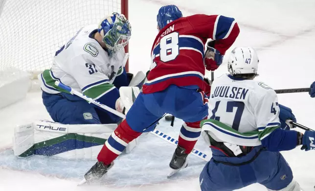 Montreal Canadiens' Lane Hutson (48) is stopped by Vancouver Canucks goaltender Kevin Lankinen (32) as Canucks' Noah Juulsen (47) moves in to defend during first-period NHL hockey game action in Montreal, Monday, Jan. 6, 2025. (Ryan Remiorz/The Canadian Press via AP)