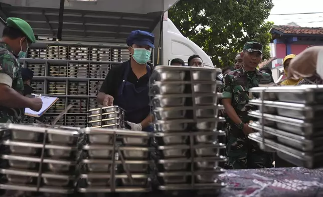 Workers unload food containers to be distributed to classrooms during the kick off of President Prabowo Subianto's ambitious free meal program to feed children and pregnant women nationwide despite critics saying that its required logistics could hurt Indonesia's state finances and economy, at an elementary school in Depok, West Java, Indonesia, Monday, Jan. 6, 2025. (AP Photo/Dita Alangkara)