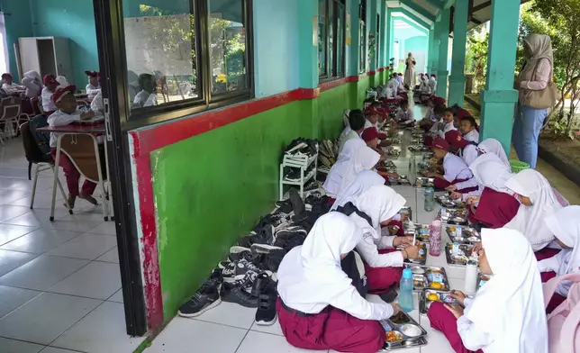 Students sit on the floor as they have their meals during the kick off of President Prabowo Subianto's ambitious free meal program to feed children and pregnant women nationwide despite critics saying that its required logistics could hurt Indonesia's state finances and economy, at an elementary school in Banten, Indonesia, Monday, Jan. 6, 2025. (AP Photo/Tatan Syuflana)