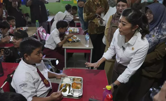 Indonesian Minister of Information and Digital Affairs Meutya Hafid, right, talks to students during the kick off of President Prabowo Subianto's ambitious free meal program to feed children and pregnant women nationwide despite critics saying that its required logistics could hurt Indonesia's state finances and economy, at an elementary school in Depok, West Java, Indonesia, Monday, Jan. 6, 2025. (AP Photo/Dita Alangkara)