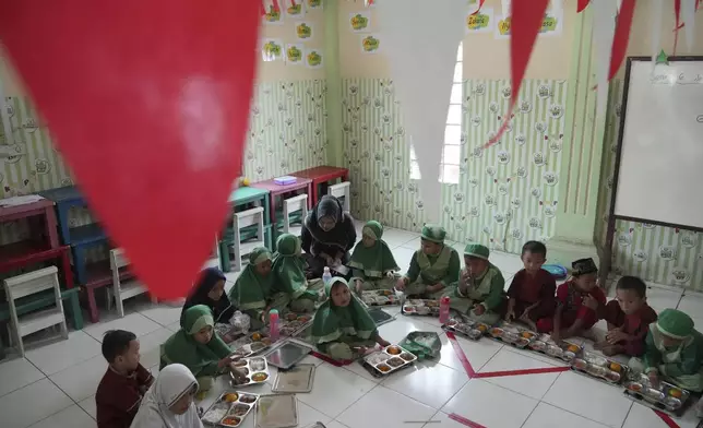 Students sit on the floor as they have their meals during the kick off of President Prabowo Subianto's ambitious free meal program to feed children and pregnant women nationwide despite critics saying that its required logistics could hurt Indonesia's state finances and economy at Early Childhood Education and Development in Jakarta, Indonesia, Monday, Jan. 6, 2025. (AP Photo/Achmad Ibrahim)